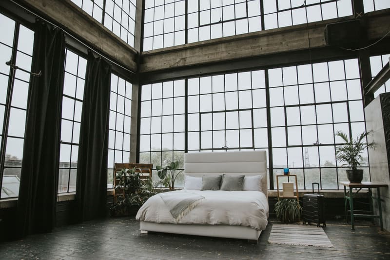 The bed made up with a grey throw in a loft with floor-to-ceiling windows