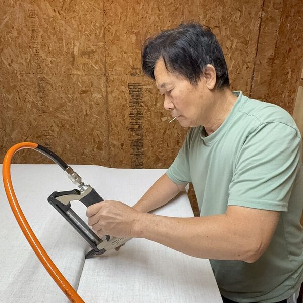 Our craftsman stapling fabric along the edge of a headboard with a pneumatic stapler