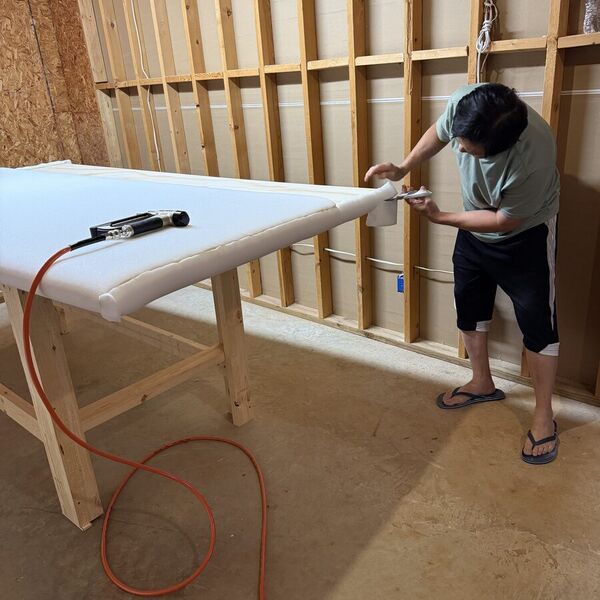 A foam-wrapped headboard panel on a workbench with a stapler, our craftsman at the far end