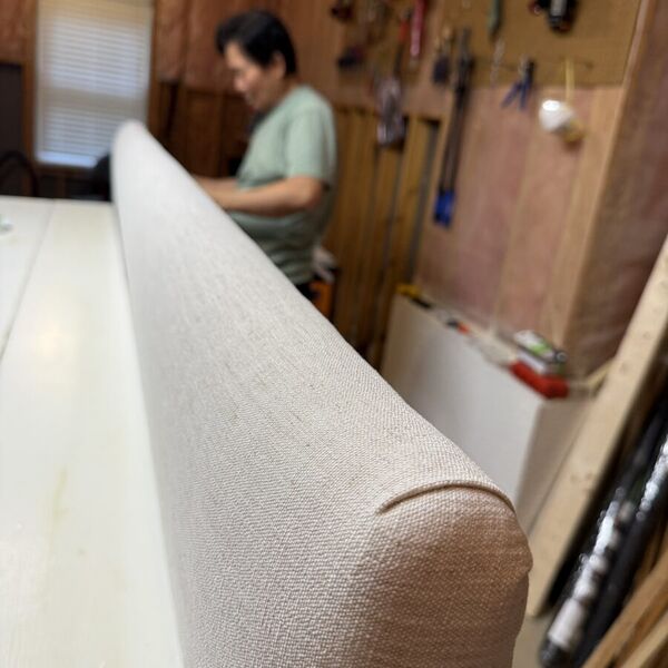 The upholstered edge of a finished headboard, our craftsman behind it